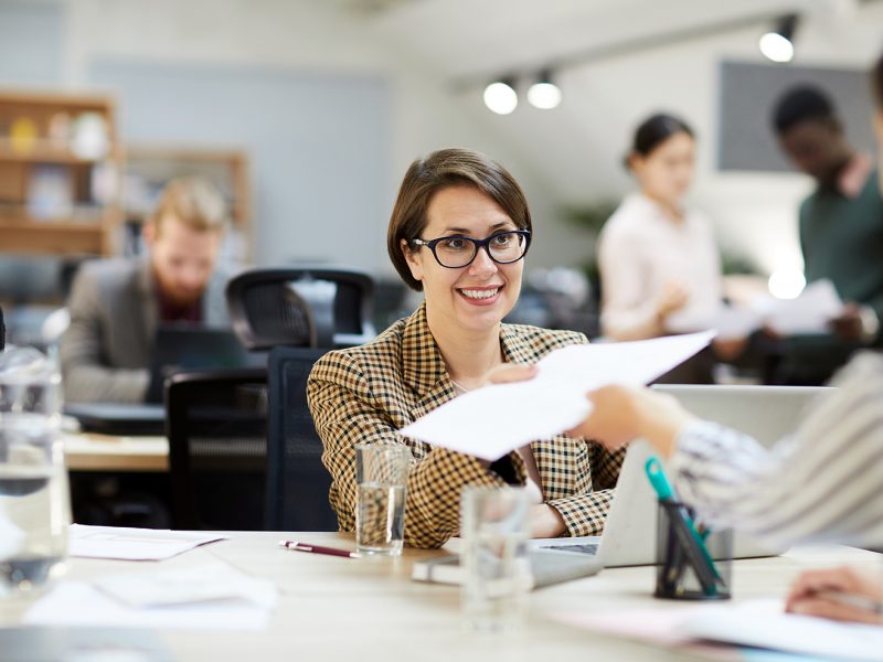 smiling-businesswoman-giving-documents-to-YLNUKBJ.jpg